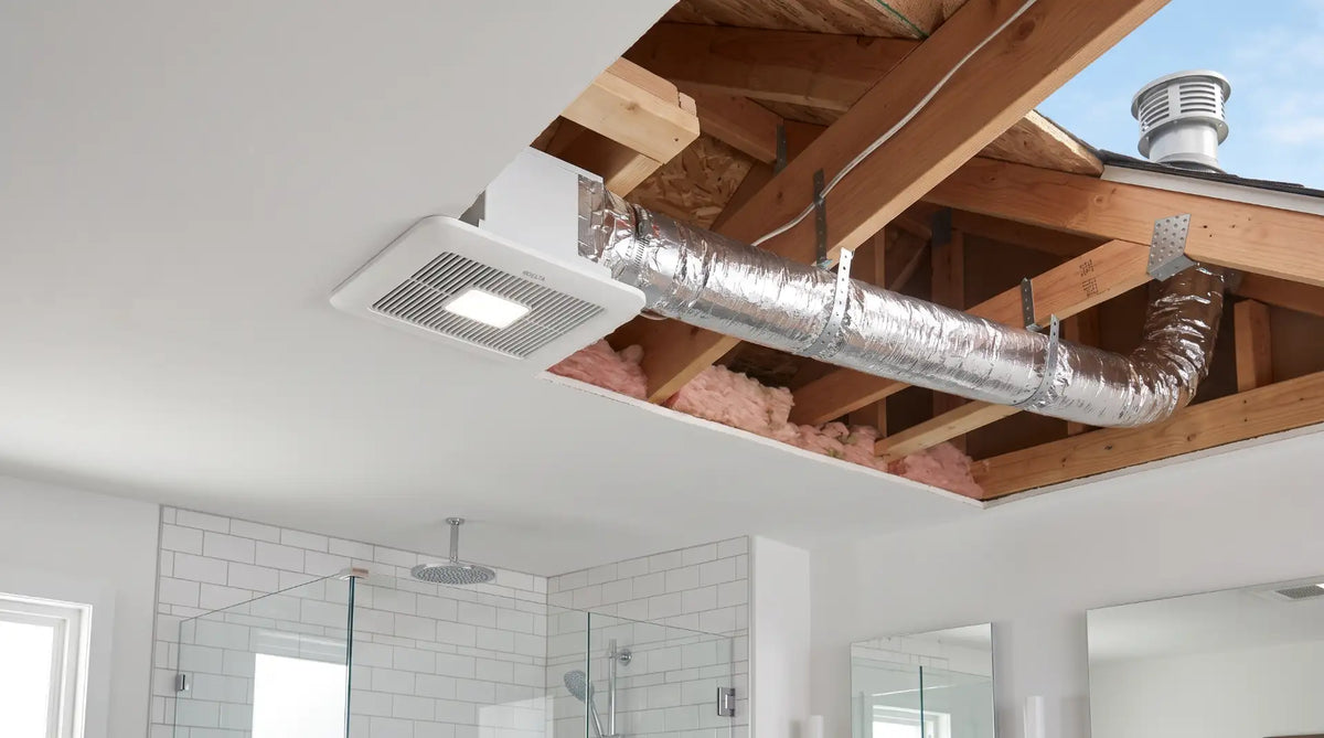 Professional installation of a bathroom exhaust fan showing insulated ductwork routed through ceiling joists for proper outdoor ventilation.